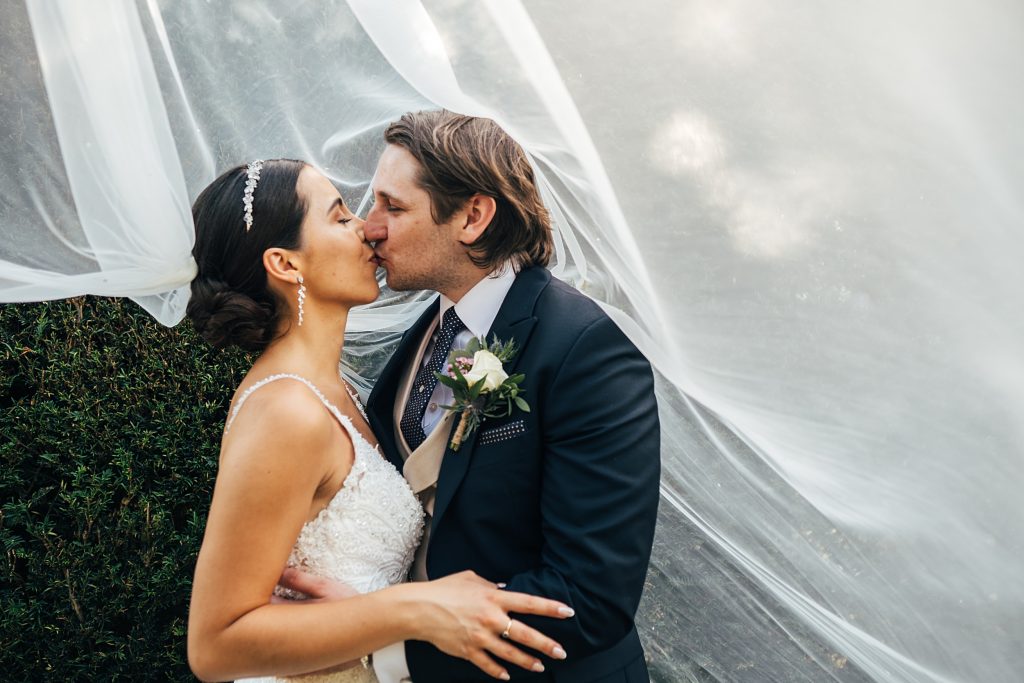 bride and groom kiss under billowing veil