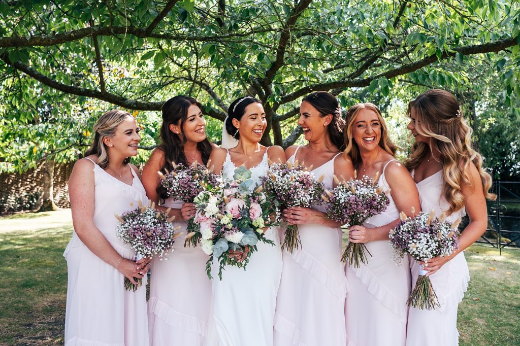 bride with bridesmaids in pink laugh under tree
