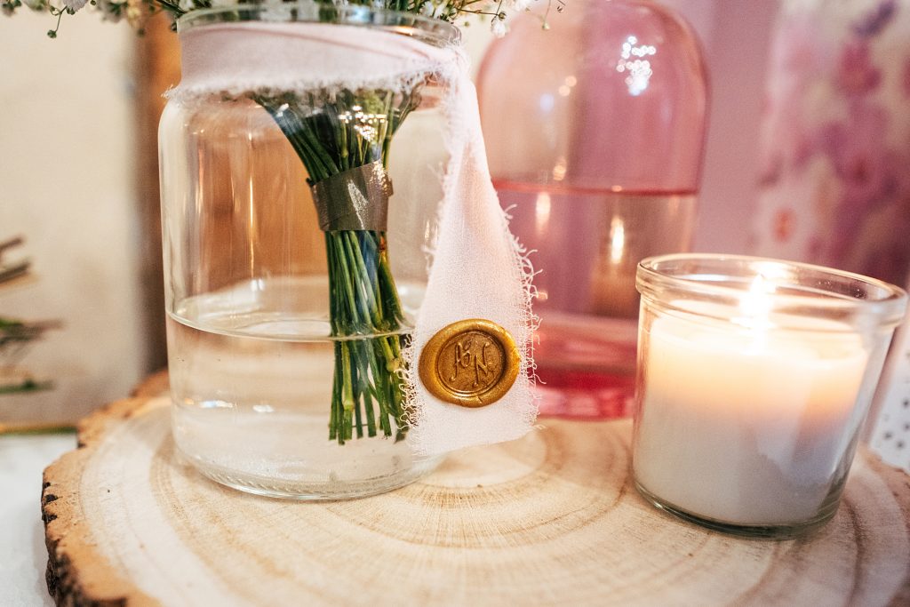 close up of pink and clear vase and candle with raw silk ribbon with gold wax seal
