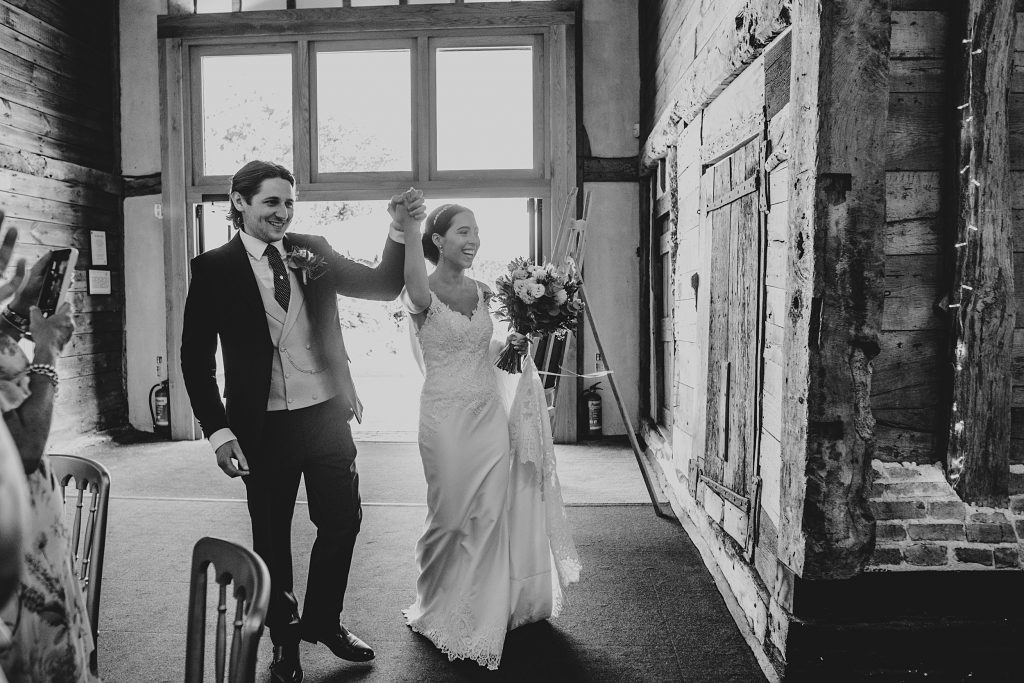 bride and groom raise arms in celebration as they enter wedding breakfast