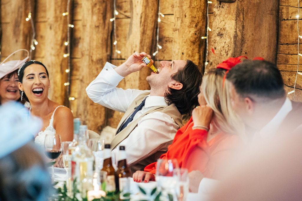 groom takes a shot from a miniature bottle during speeches
