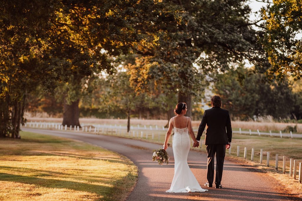 bride and groom walk down tree lined driveway at sunset