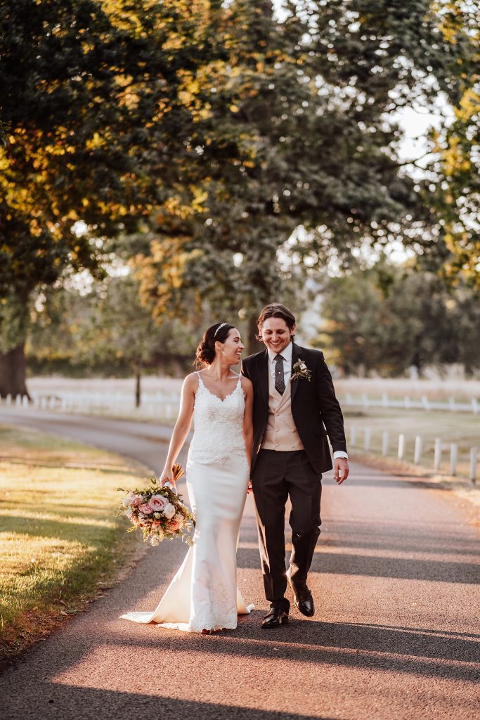 bride and groom walk treelined driveway at sunset