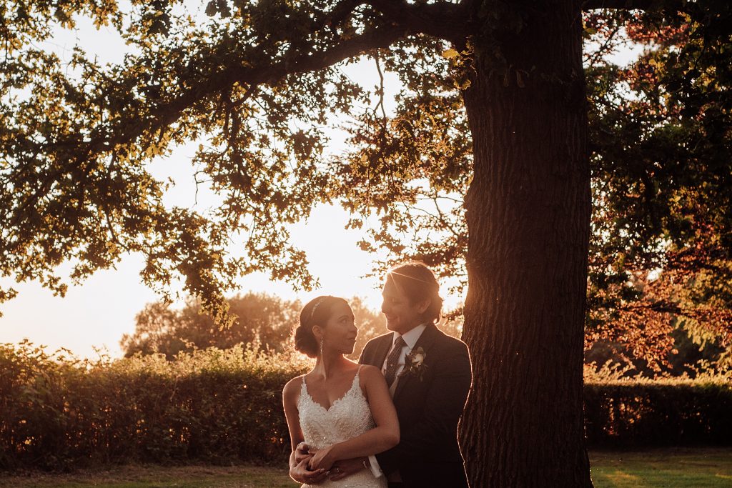 bride and groom under big oak at sunset