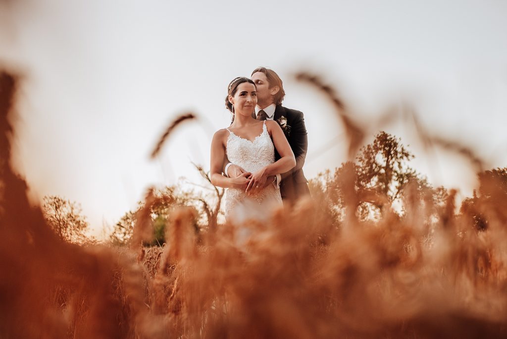 bride and groom in wheat field at sunset