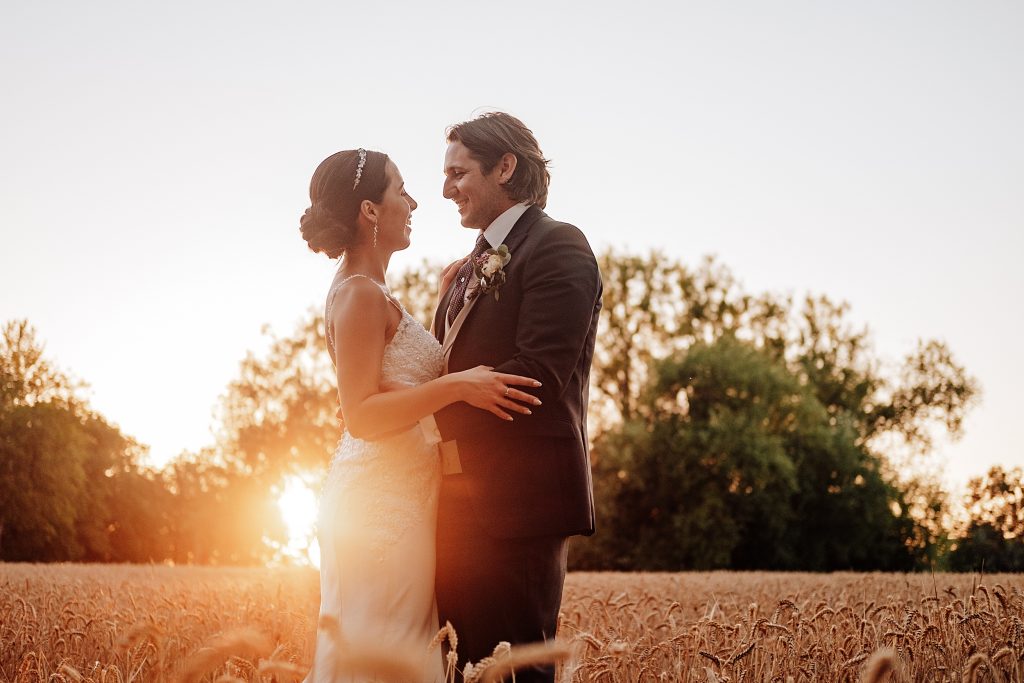 bride and groom laugh in wheat field at sunset