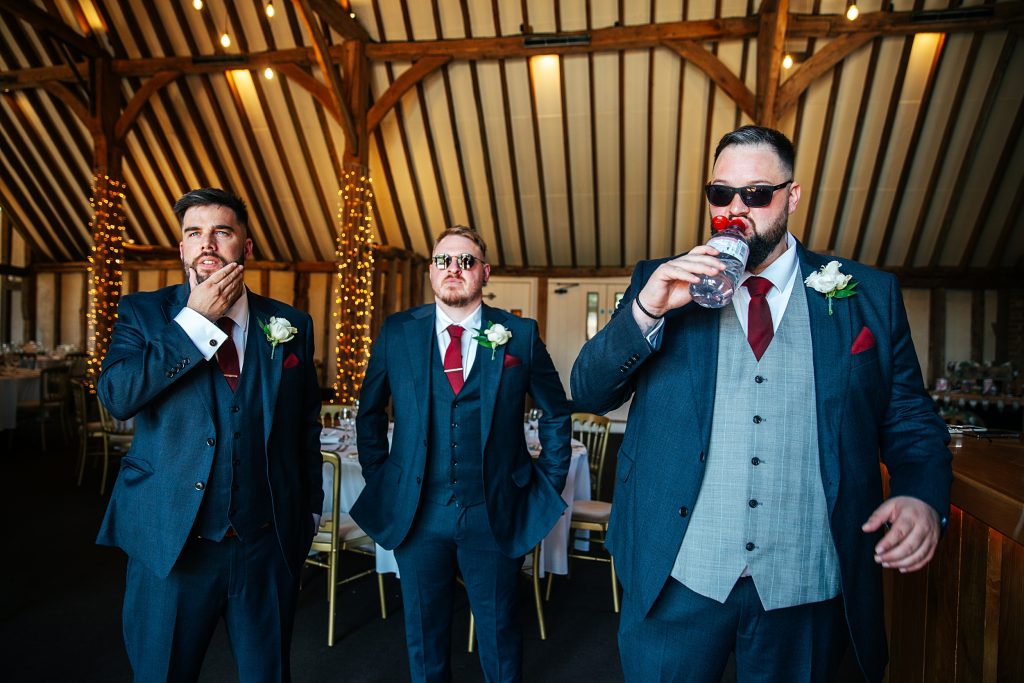 groom drinks from bottle of water as he stands with best men