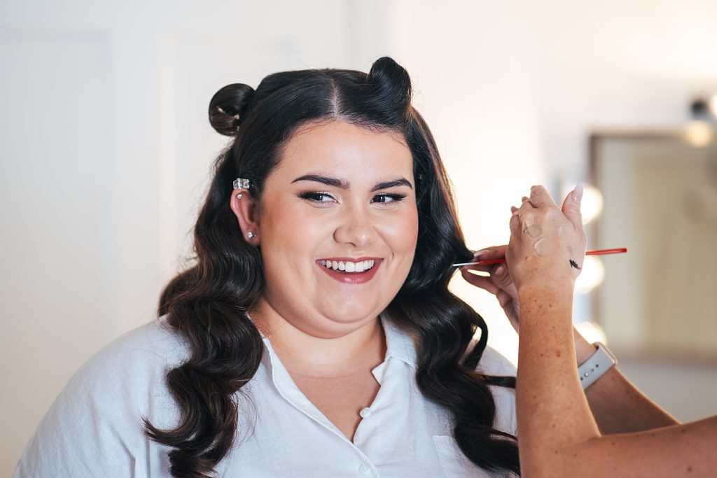 smiling bride with hair in curlers has make up applied