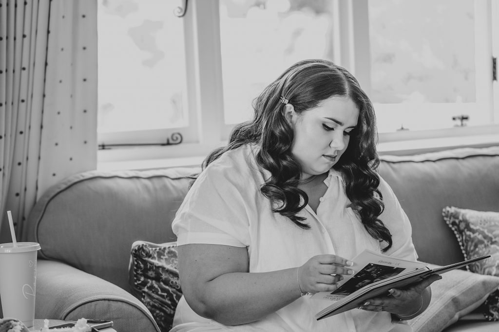 bride in white pyjamas sits on sofa and looks through a book