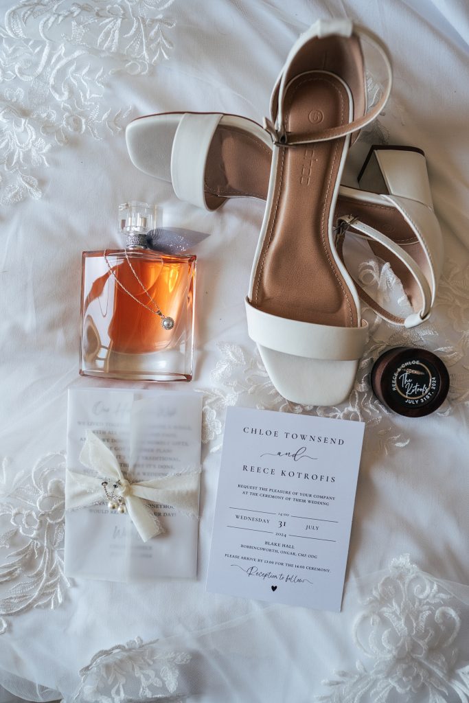 flat lay of bridal shoes, invitation, perfume and necklace