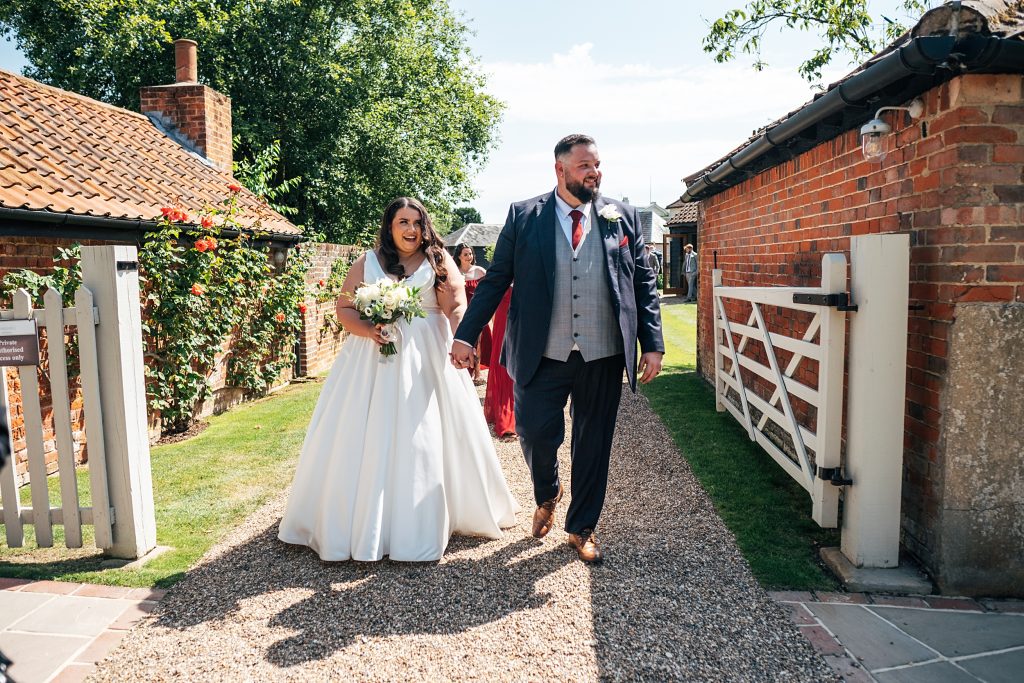 bride and groom walk through gate to drinks reception