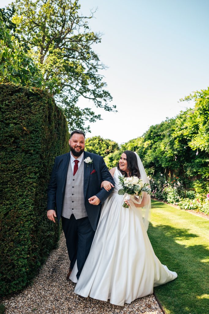 Bride and groom laugh and walk in gardens at Blake Hall