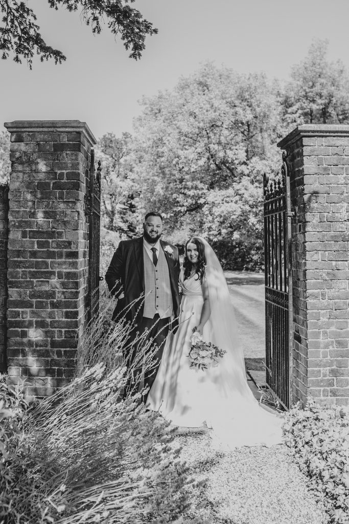Bride and groom stand in gateway to walled gardens at Blake Hall