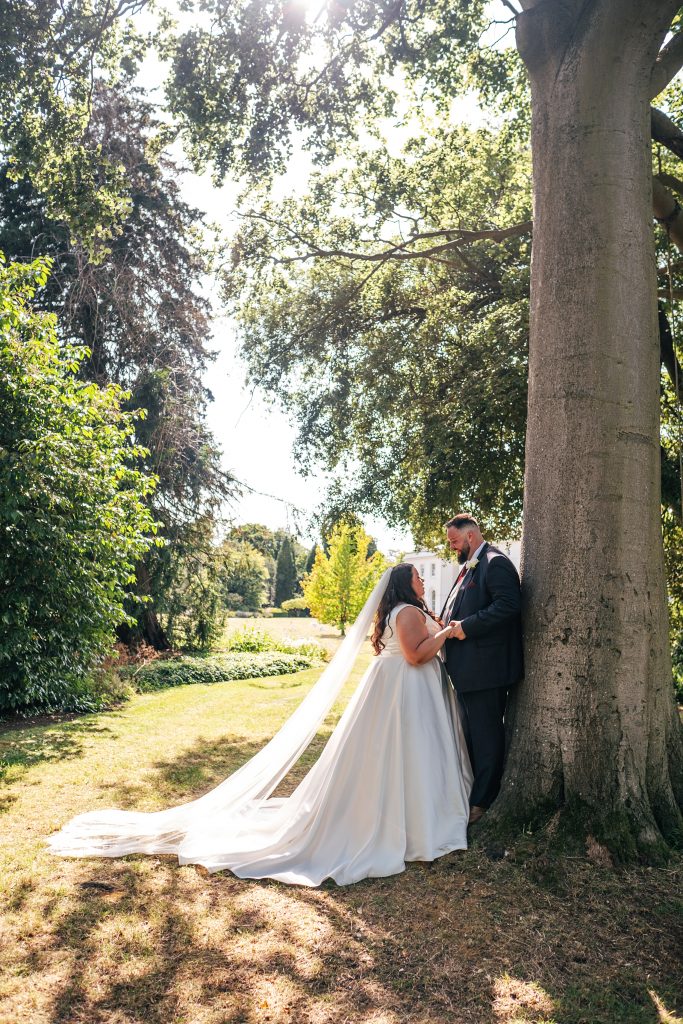 bride and groom stand next to huge oak tree in garden