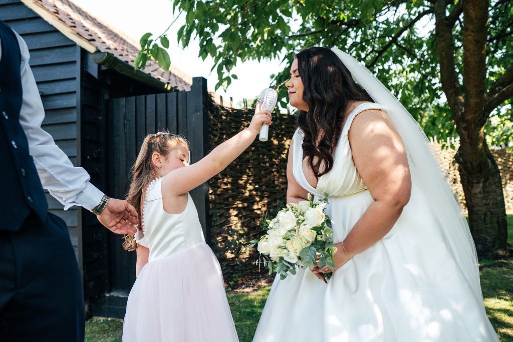 flower girl holds up fan to brides face