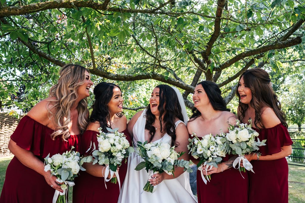 bride and bridesmaids in red laugh under a tree