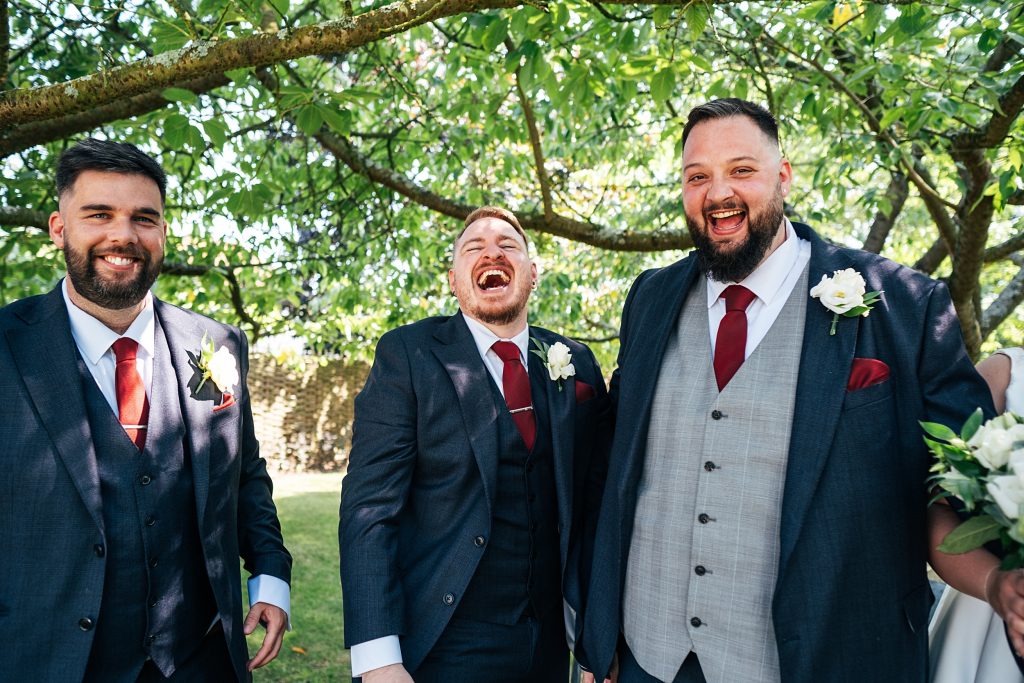 groom and groomsmen laugh under a tree