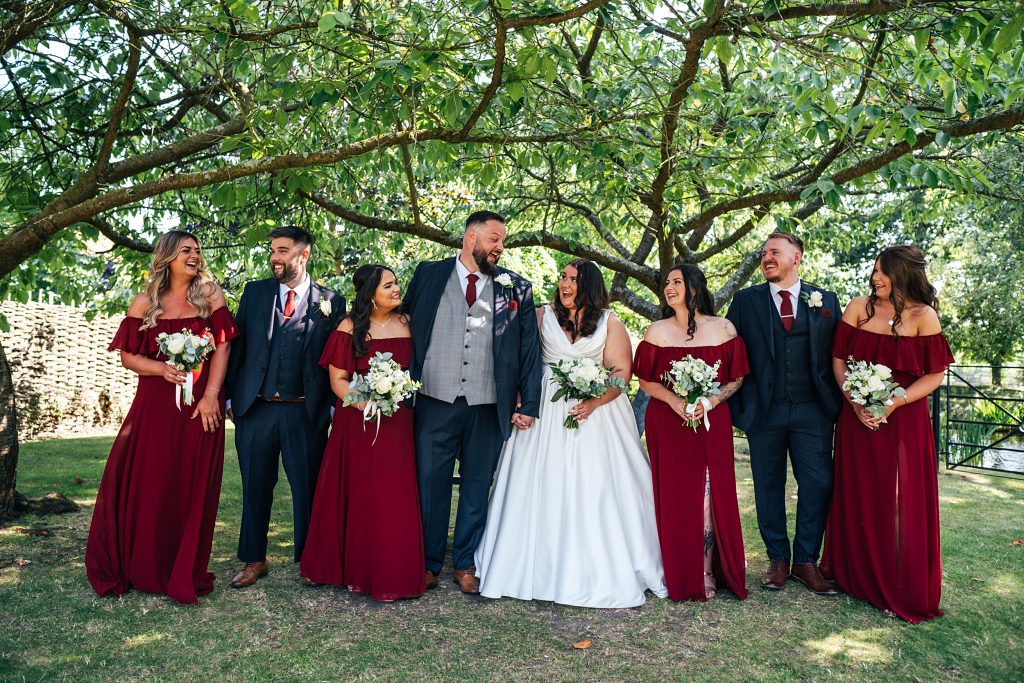 bride groom and wedding party laugh under a tree