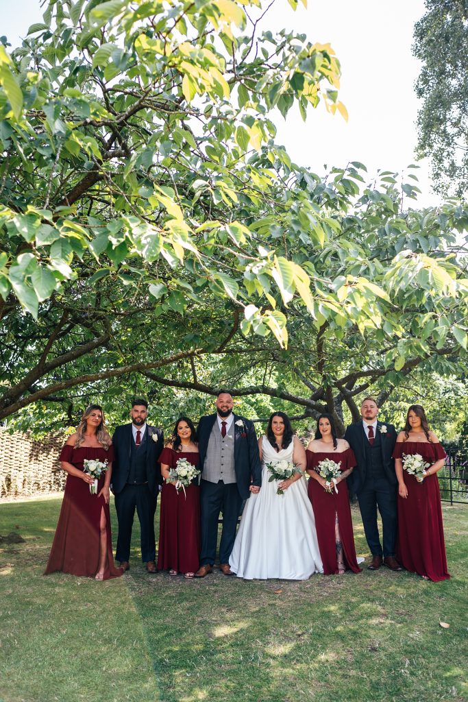 bride and groom with wedding party stand under a tree