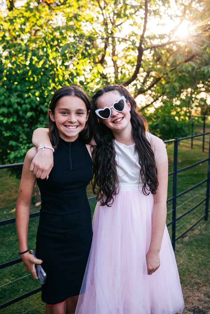 flower girl in white heart sunglasses hugs friend in garden