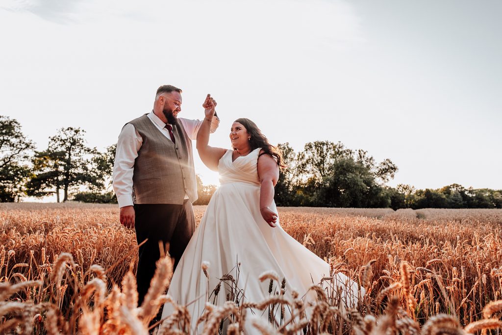 groom spins bride in wheat field at sunset