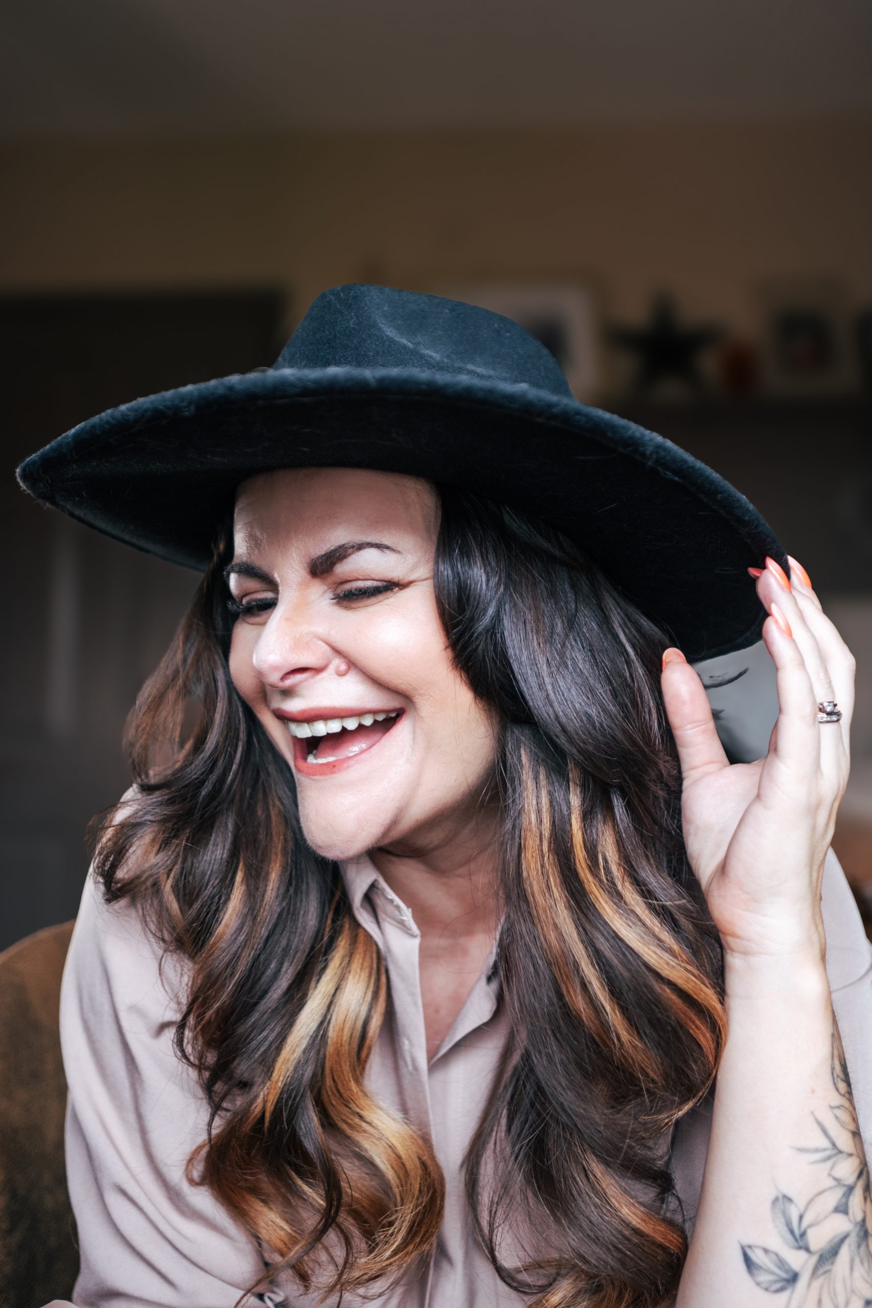 Woman with long dark hair laughs as she holds onto edge of black hat