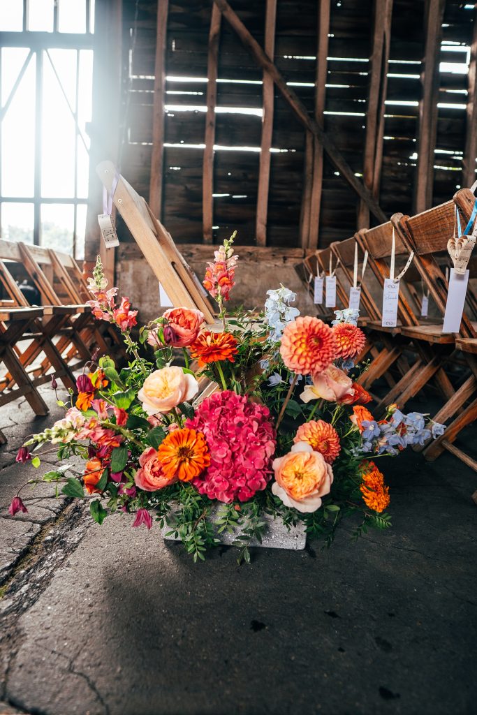 Pinks, Orange and purple floral display at end of seating row in barn