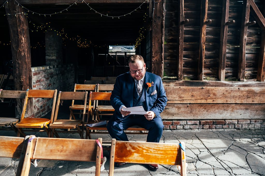 groom sits in rustic old barn adorned with fairy lights and reads a letter from his bride