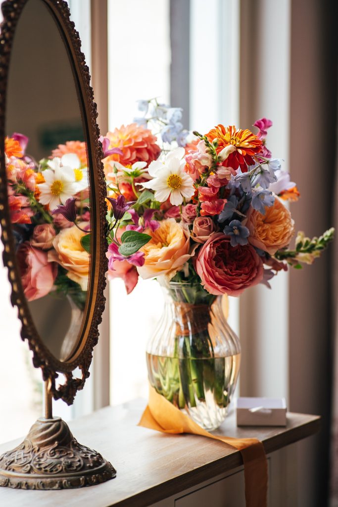brides bouquet of pinks and oranges sits in a vase in bridal prep room