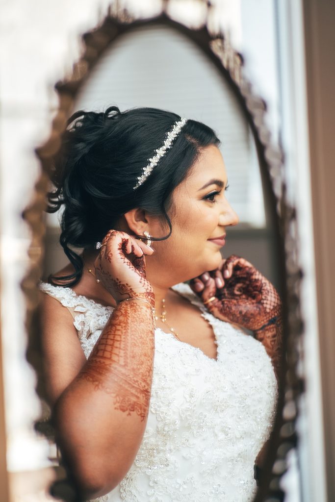 bride adjusts earrings in mirror, she bridal henna on her hands and arms