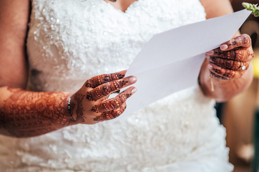 close up of brides hands, decorated with henna as she holds letter from groom