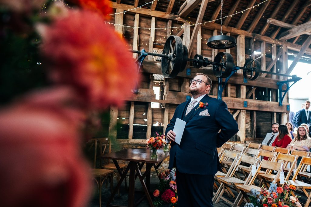 groom looks nervous as he waits for bride in rustic barn