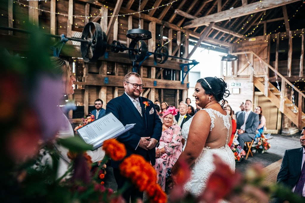 bride and groom smile during wedding ceremony in rustic barn