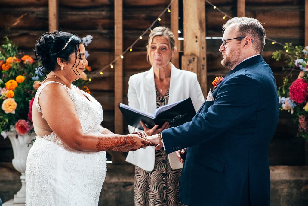 bride and groom hold hands during ceremony in rustic barn