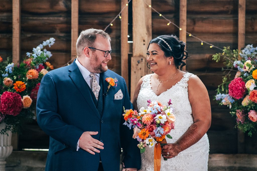 bride and groom laugh as they wait to walk back up aisle in rustic barn