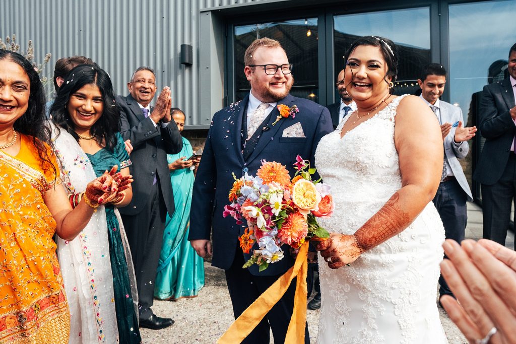 laughing bride and groom stand with guests covered in confetti