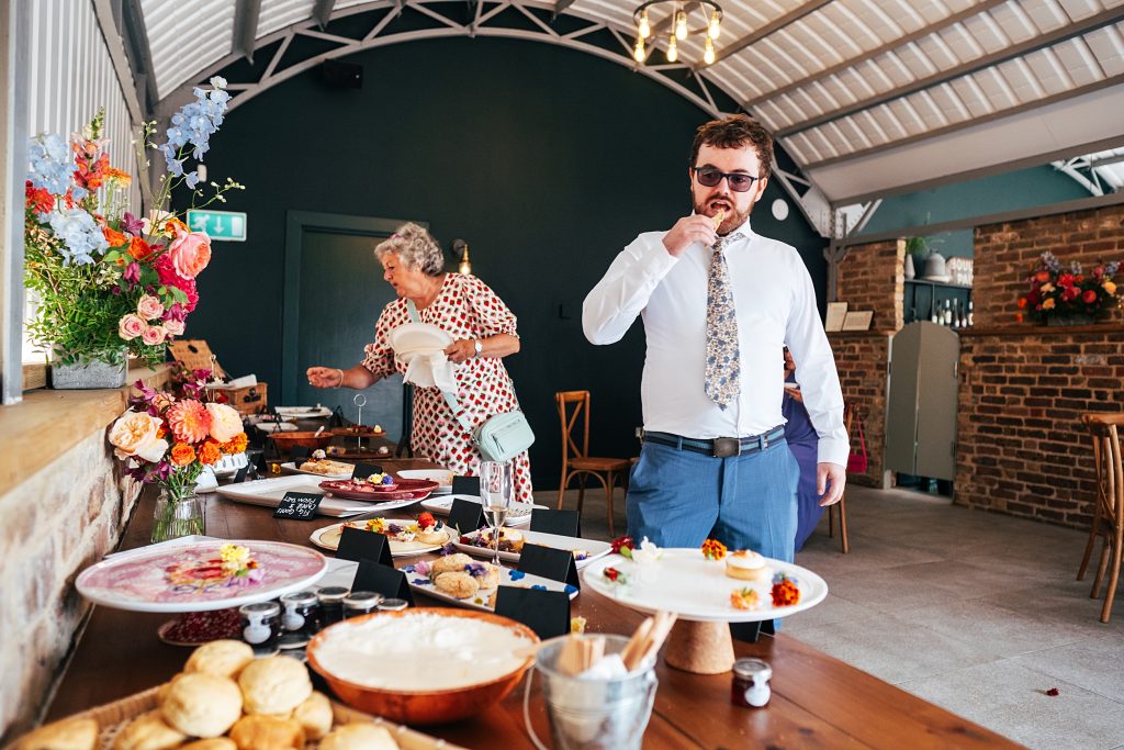 wedding guests serve themselves afternoon tea in barn with arched roof