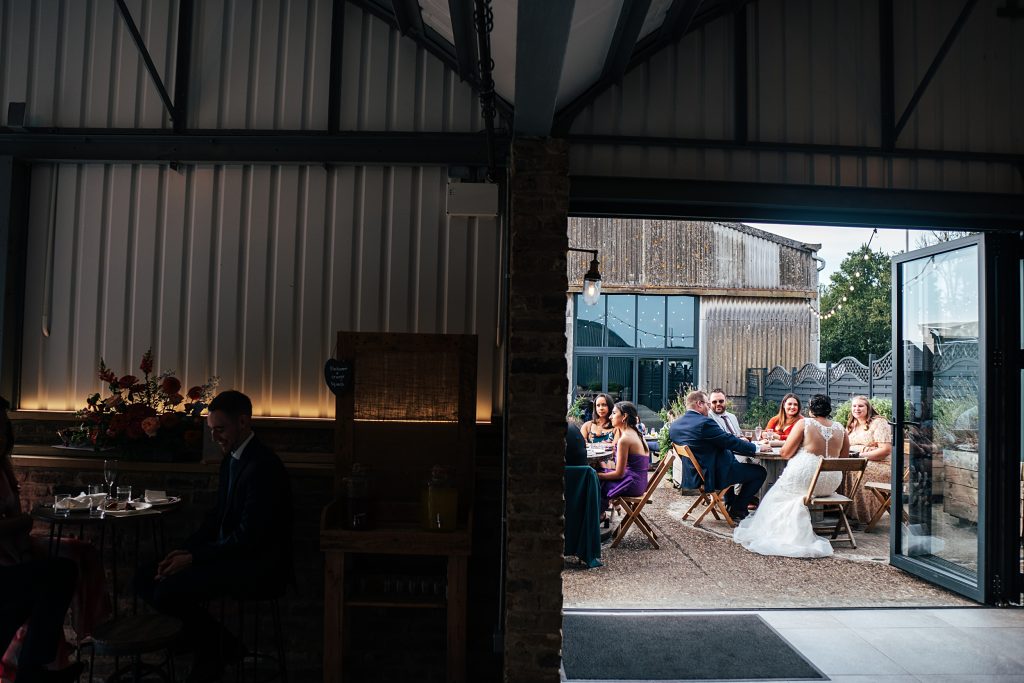 view of wedding guests sat at outdoor tables from inside barn