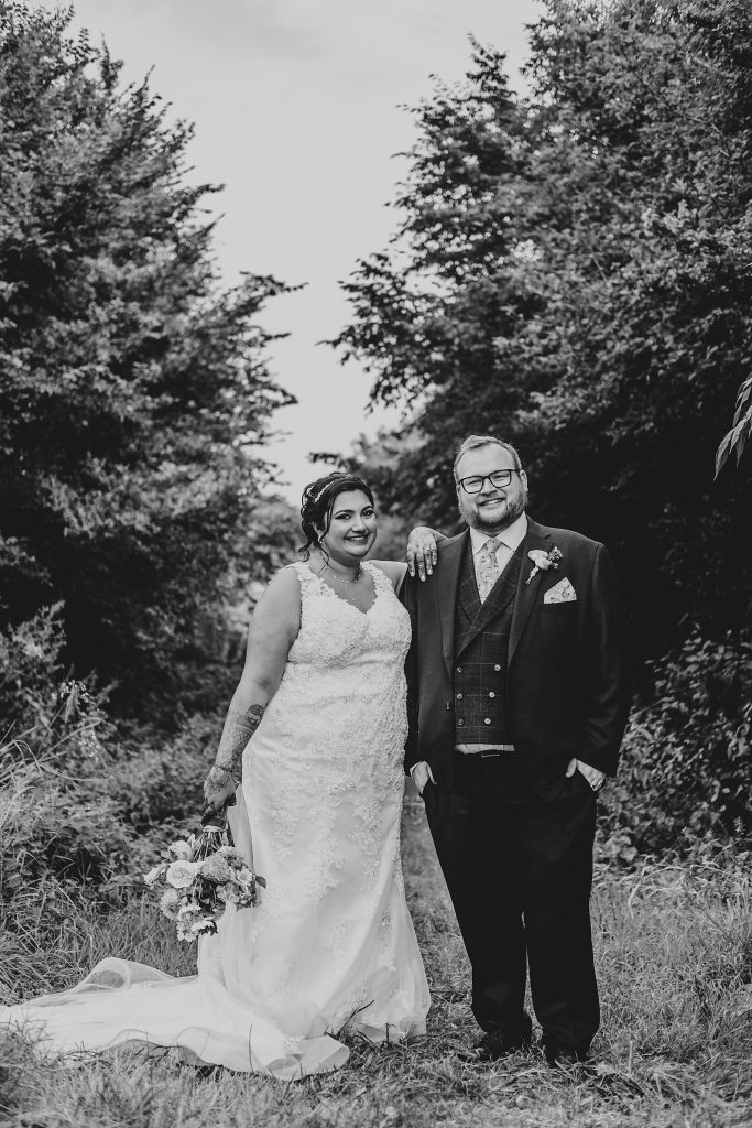 bride leans on grooms shoulder as the both smile at camera in a field