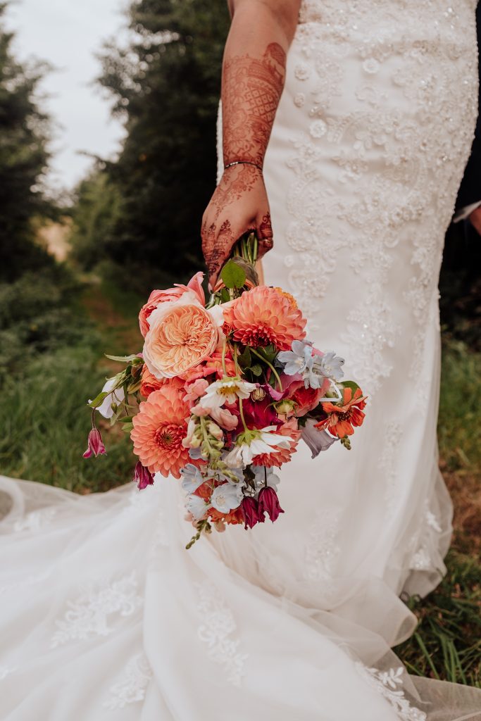 close up of bride holding pink and orange bouquet, her hands are decorated with henna