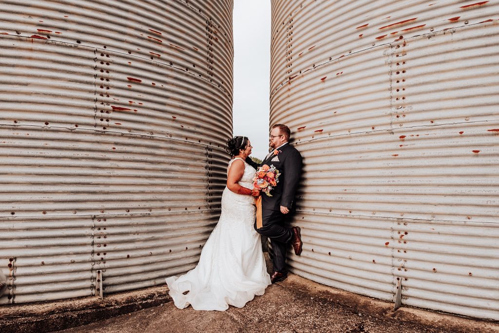 bride and groom stand inbetween two grain silos
