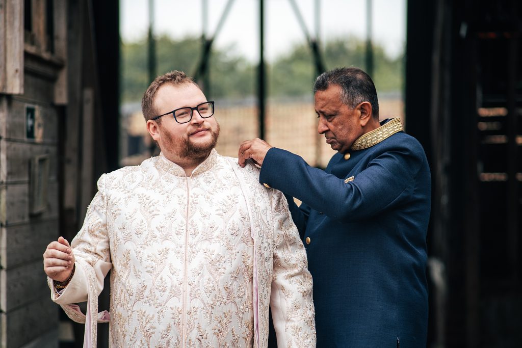 Groom has his suit adjusted outside a barn