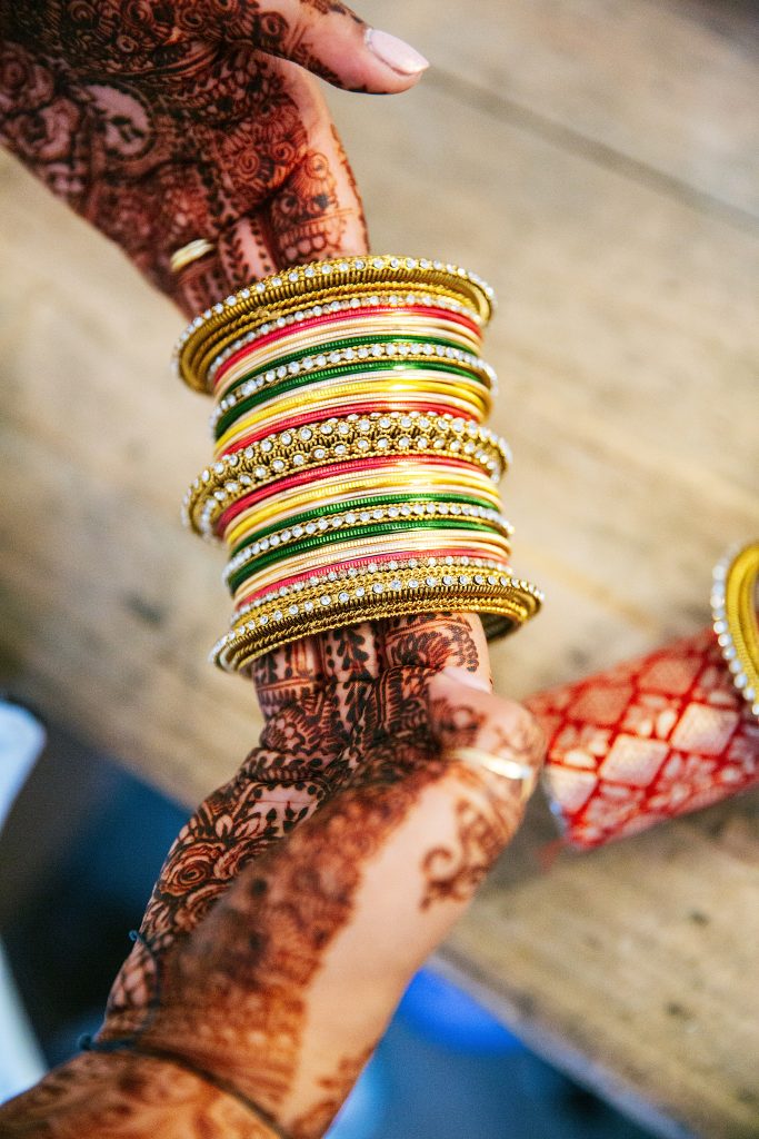 close up of bride's henna'd hands holding gold bangles