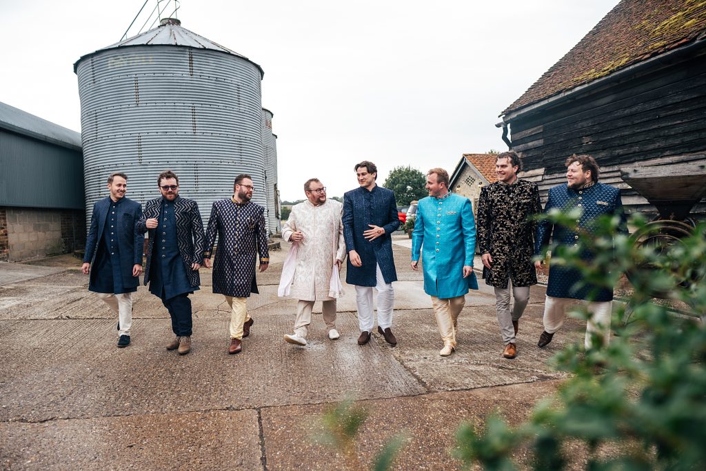 Groom and groomsmen in Sherwanis walk in the courtyard at Barns at Lodge Farm