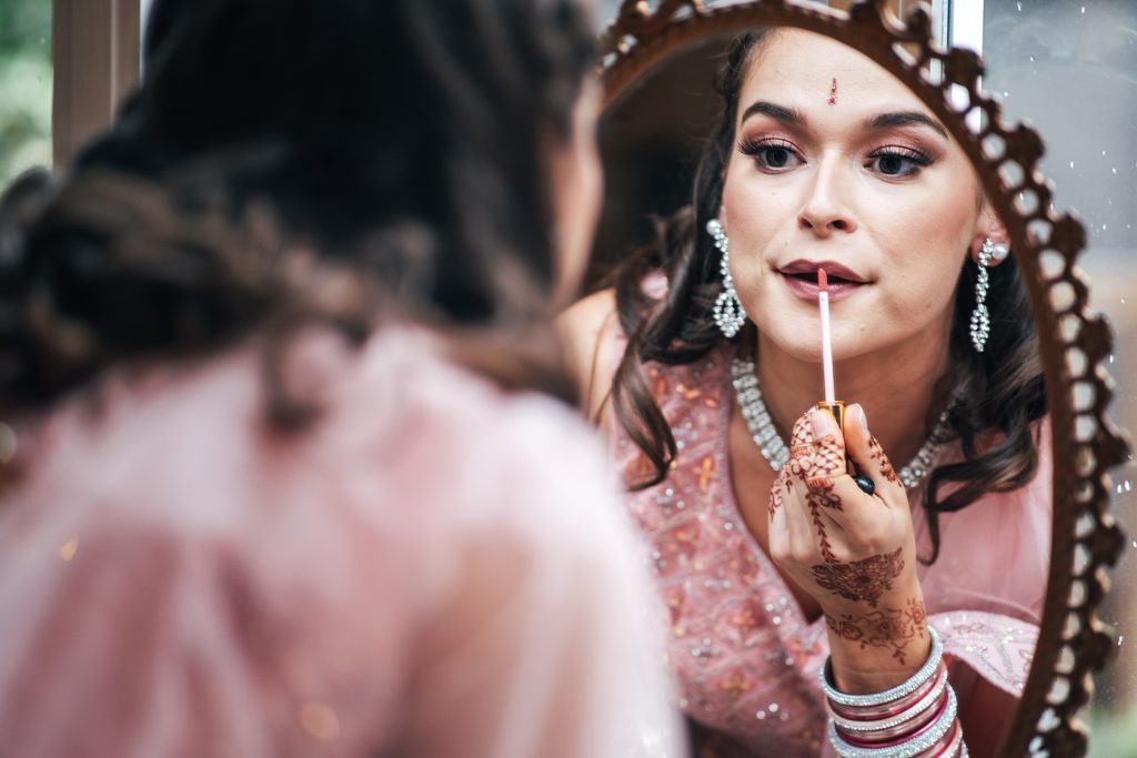 guest in traditional sari with bindi puts on lip gloss in mirror