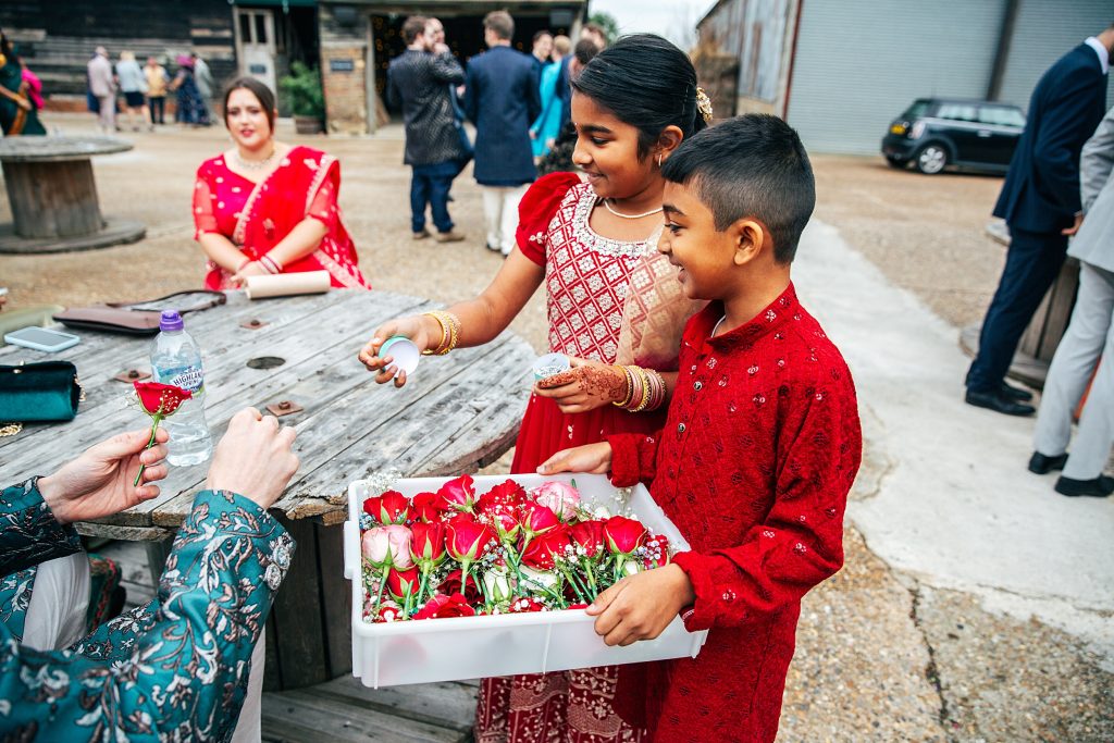 two children in red and gold hand out red roses to guests