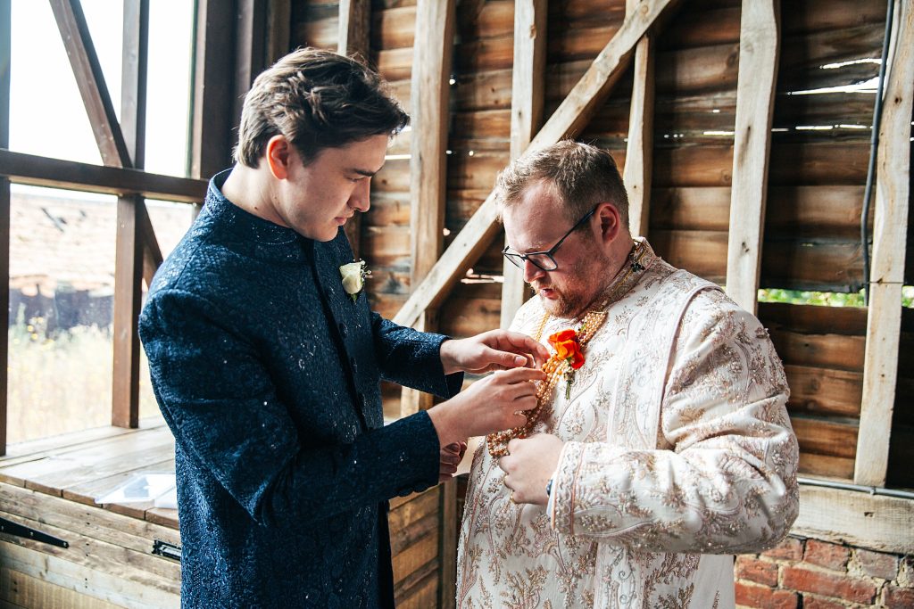best man helps groom with button hole in barn