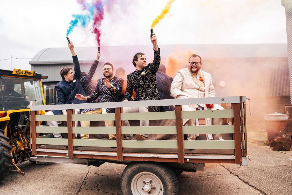 Groom and groomsmen arrive for Jaan on tractor holding colourful smoke bombs