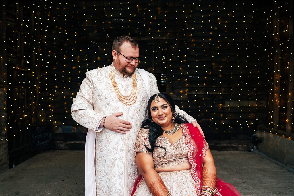 bride and groom sit in fairy light lit shed in farm