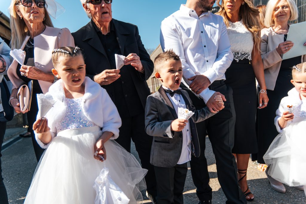 Little boy in black tie is excited to throw confetti at The Barns at Lodge Farm Essex documentary wedding photographer